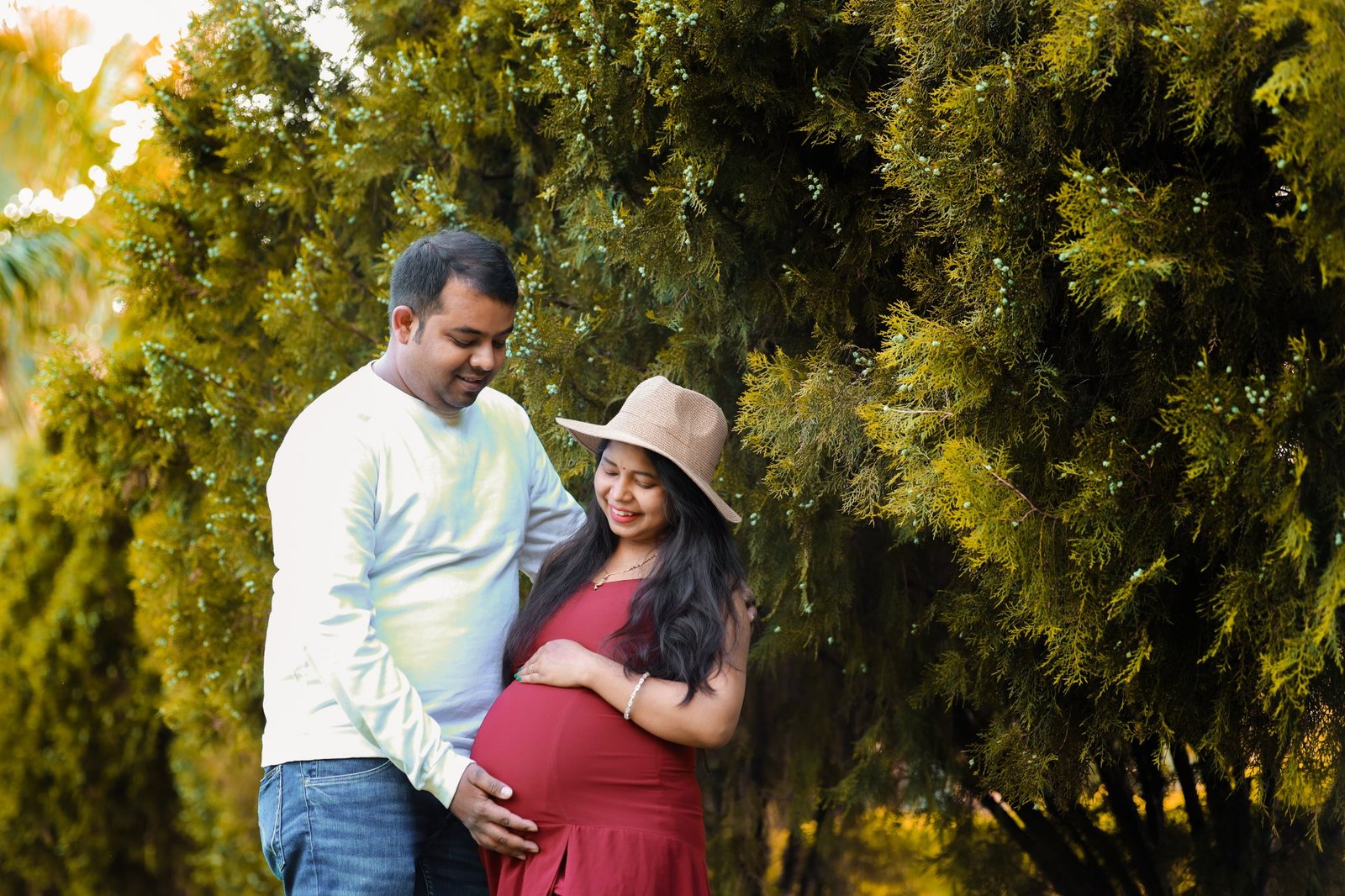 Expectant mother in a fitted red dress photographed outdoors with her partner