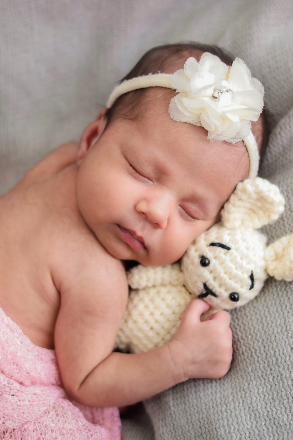 Newborn in a pink wrap holding a small knitted bear